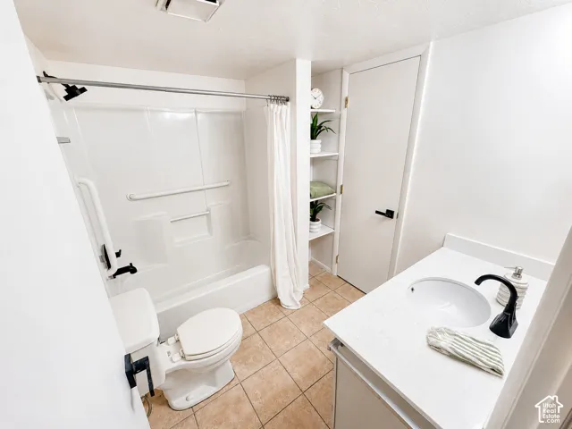 White vanity with a single basin sink and a matte black faucet, white shower/tub combination with grab bars, toilet with a bidet attachment, and built-in shelving