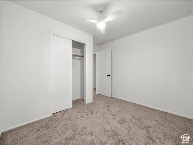 Neutral toned carpeting, contemporary ceiling fan, white walls, and a built-in closet with sliding doors