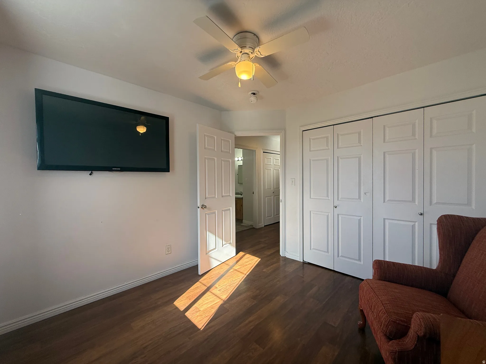 Wood-finish flooring, ceiling fan with integrated lighting, built-in wall-mounted television, and bi-fold closet doors