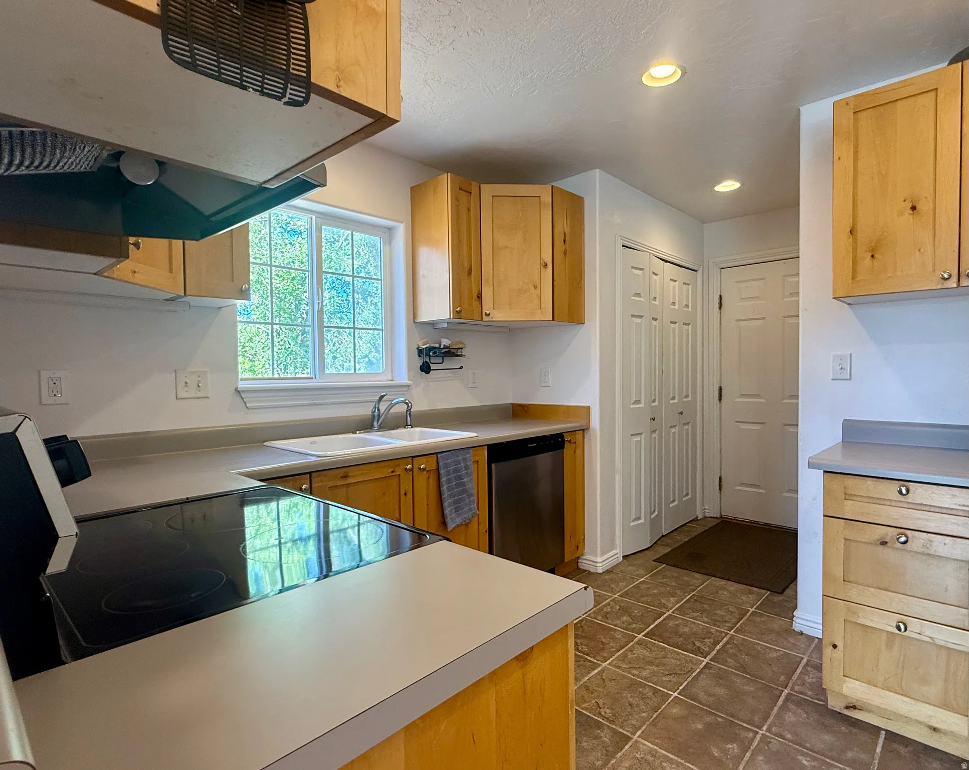 Kitchen featuring wood cabinetry, a double basin sink, stainless steel dishwasher, tile flooring, and recessed lighting
