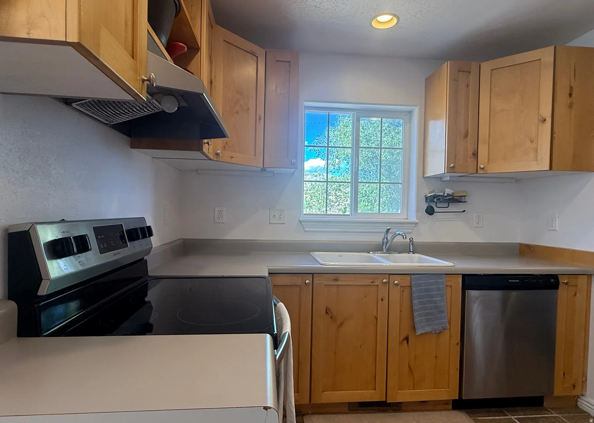Kitchen featuring wood cabinetry, stainless steel dishwasher, dual basin sink, and an electric range