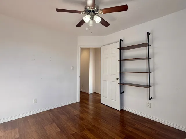 Wood-finish flooring, ceiling fan with integrated lighting, and a built-in wall shelf with dark-toned wood shelves and black metal supports