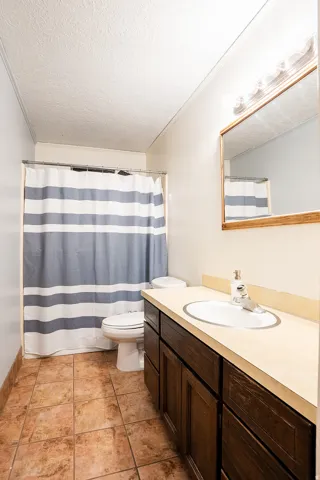 Tile flooring, dark wood-finish vanity, integrated sink, wall-mounted mirror, and vanity lighting