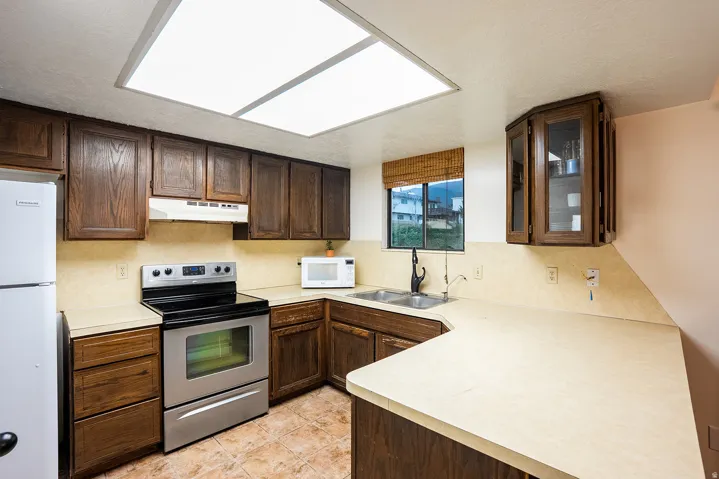 Kitchen featuring wood cabinetry, light-toned countertops, stainless steel appliances, and tile flooring