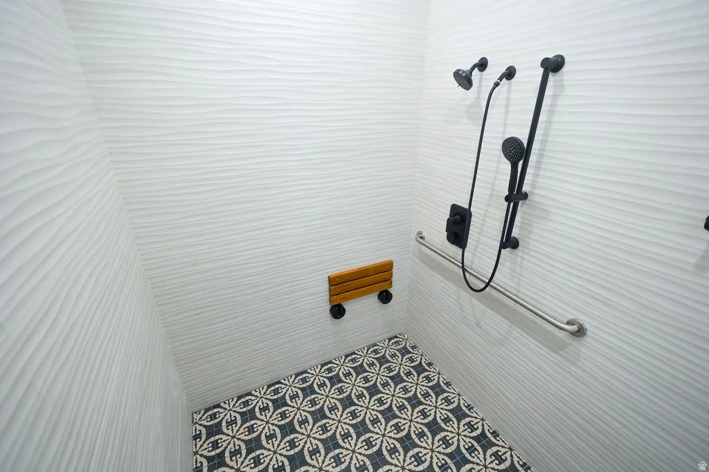 Shower featuring textured wall tile, patterned floor tile, matte black shower fixtures, a built-in shower seat, and a grab bar