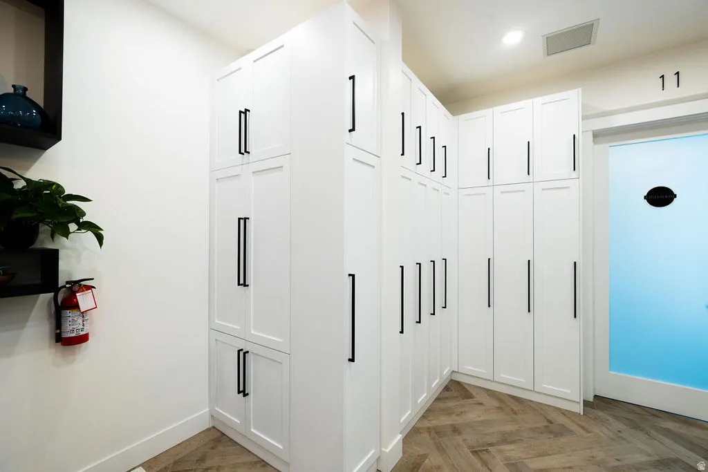 White cabinetry with matte black hardware, wood-finish flooring in a herringbone pattern, and recessed lighting