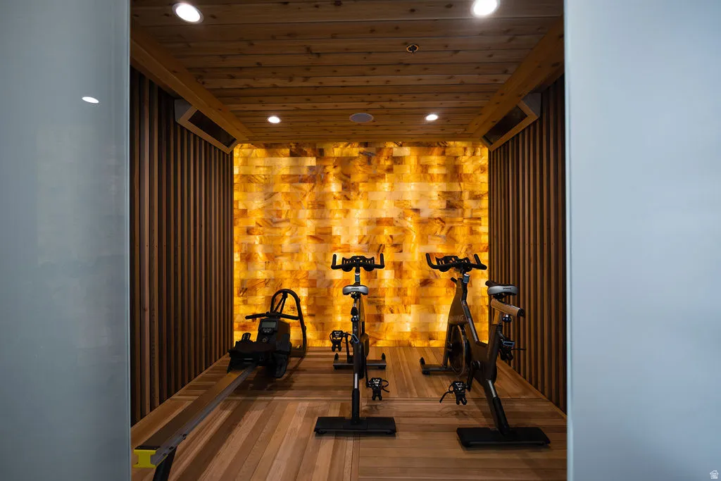 Wood-paneled ceiling with recessed lighting, illuminated accent wall, wood-finish flooring, and vertical wood-slat wall paneling