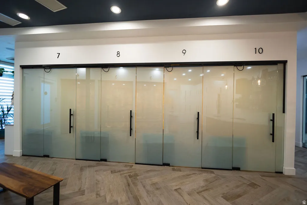 Four glass panel sliding doors with matte black hardware, recessed lighting, and wood-finish flooring in a herringbone pattern