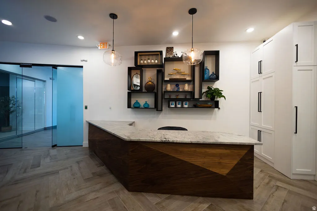 Herringbone-patterned wood-finish flooring, a multi-paneled wood reception desk with a stone countertop, built-in display shelving, and full-height white cabinetry with black hardware