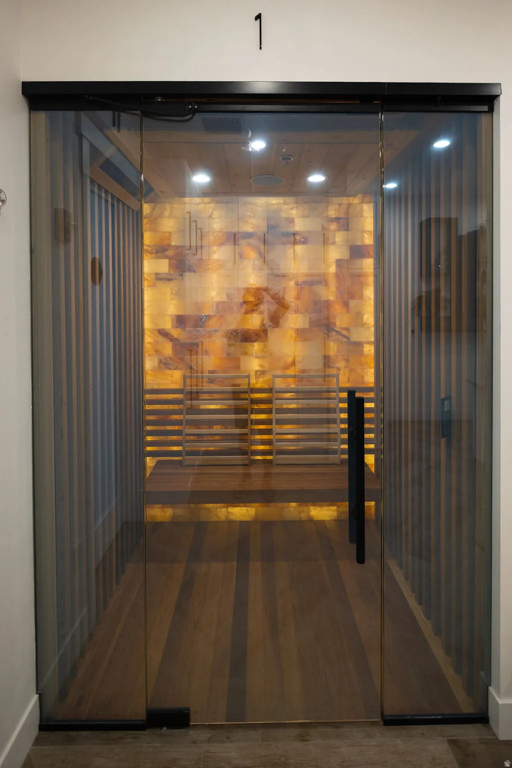Glass entry door with a matte black handle, wood-finish flooring, and an illuminated stone-clad wall