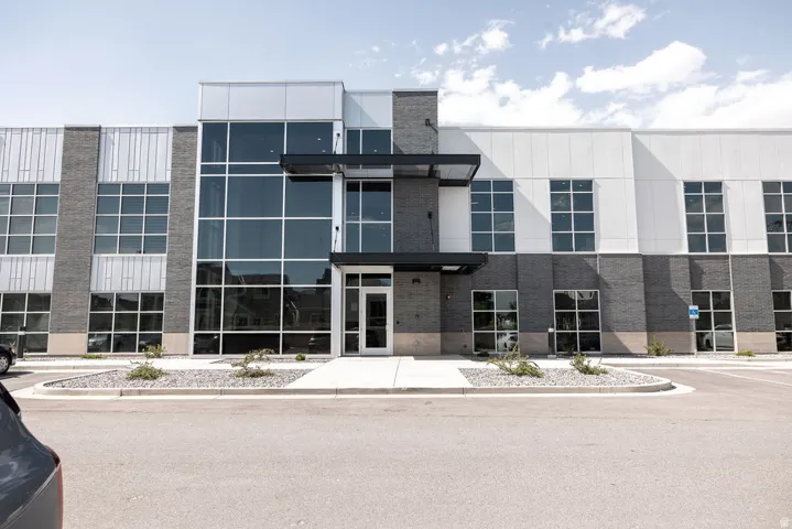 Modern commercial building featuring a brick and panel facade, large glass windows, a prominent glass entry, and a paved parking area