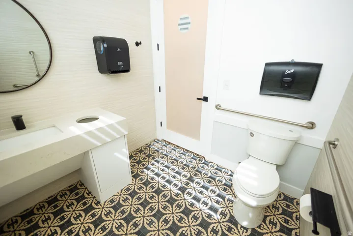 Patterned floor tile, white vanity with integrated sink, circular wall mirror, and white toilet