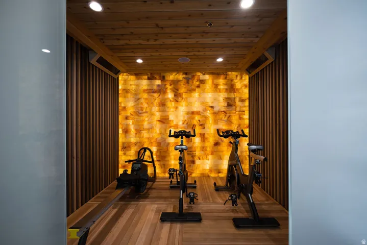 Wood-paneled ceiling with recessed lighting, illuminated accent wall, wood-finish flooring, and vertical wood-slat wall paneling