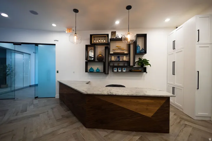 Herringbone-patterned wood-finish flooring, a multi-paneled wood reception desk with a stone countertop, built-in display shelving, and full-height white cabinetry with black hardware