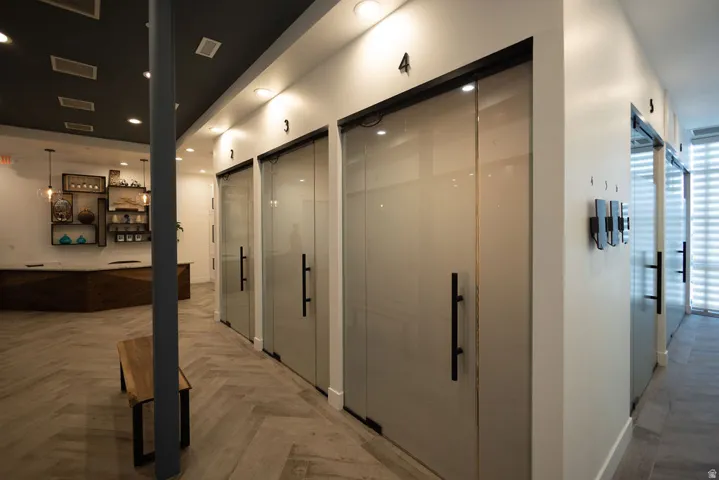 Herringbone wood-finish flooring, recessed lighting, individual glass panel doors, geometric wood reception desk, and decorative wall shelving