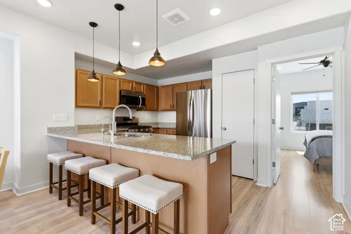 Kitchen featuring an island with a stone-finish countertop, wood-finish cabinetry, stainless steel appliances, and pendant lighting