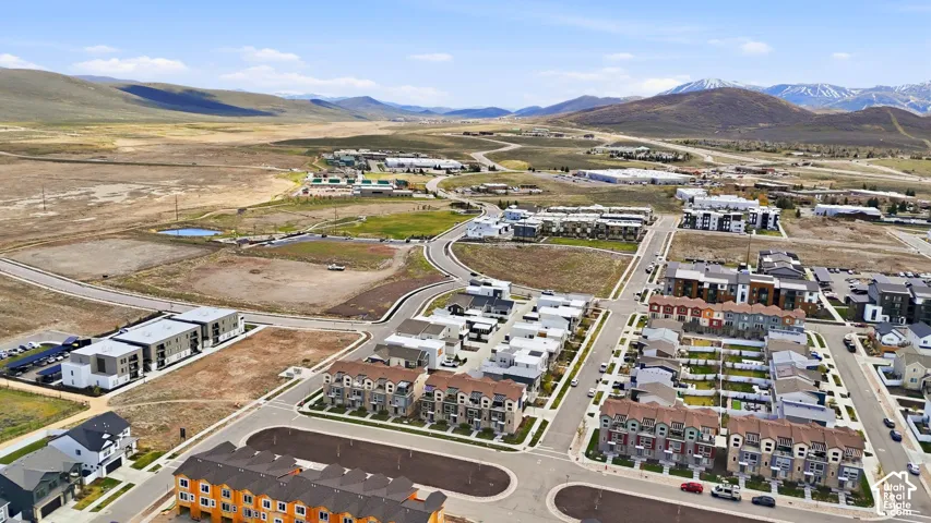 Aerial perspective of a multi-unit residential community featuring paved thoroughfares, attached townhomes, and a backdrop of expansive mountain ranges
