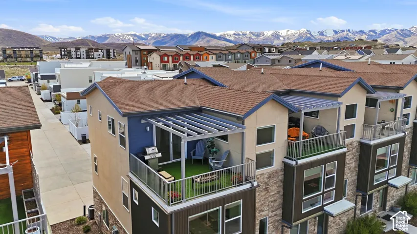 Multi-level residential exterior featuring stone veneer siding, dual upper-level balconies with metal railings, and attached pergolas, set against a mountain backdrop