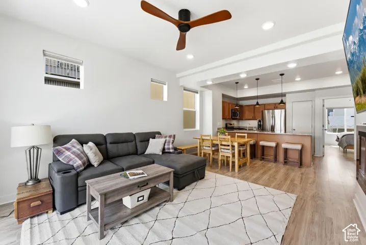 Open-concept interior featuring wood-finish flooring, a contemporary three-blade ceiling fan, recessed lighting, and kitchen cabinetry with a breakfast bar