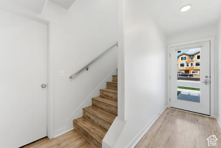 Entryway featuring wood-finish flooring, a staircase with matching wood-finish treads, a brushed metal handrail, and a door with an integrated glass panel