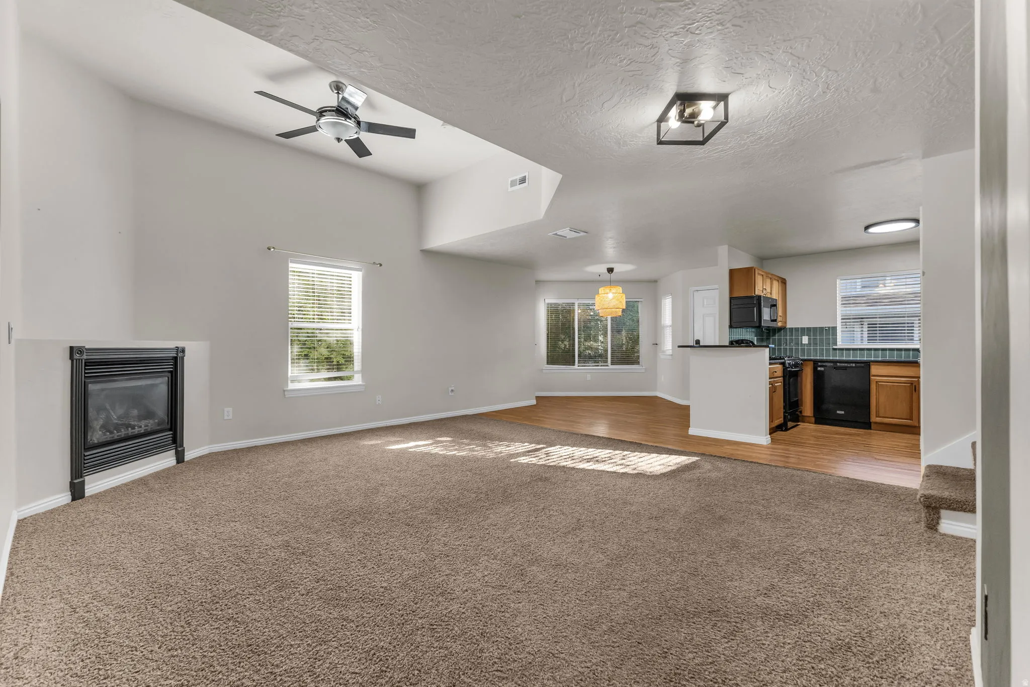 Vaulted ceiling with ceiling fan, built-in fireplace, wood-finish flooring, and kitchen with wood cabinetry and black appliances
