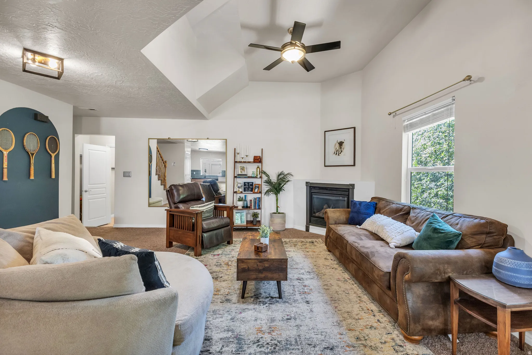 Vaulted ceilings with ceiling fan, corner fireplace, large window with natural light, and built-in shelving unit