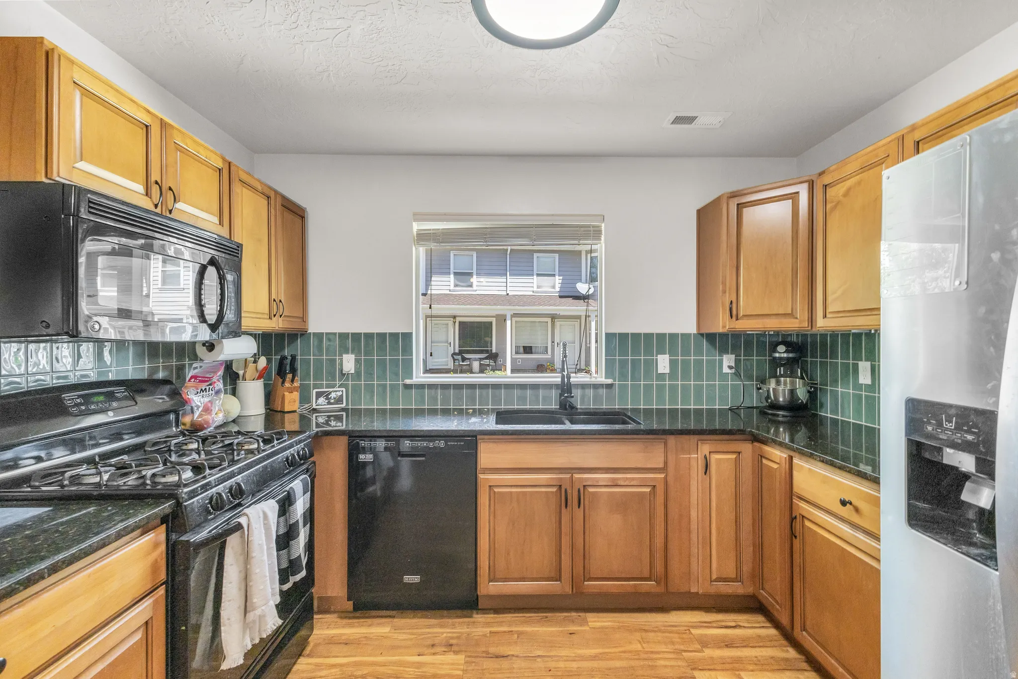 U-shaped kitchen featuring wood cabinetry, dark countertops, a tile backsplash, and wood-finish flooring