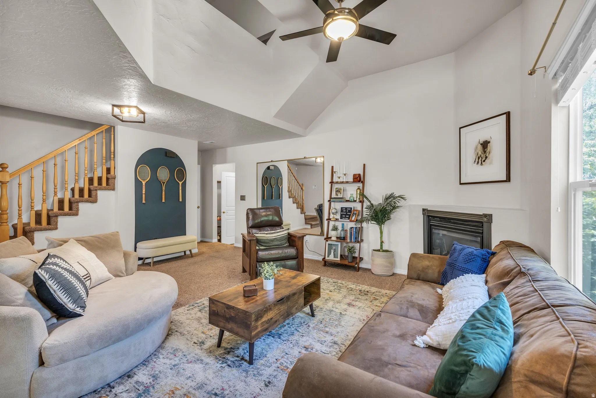 Vaulted ceilings with ceiling fan, built-in fireplace, wood staircase with balusters, large window, and wall-mounted light fixtures