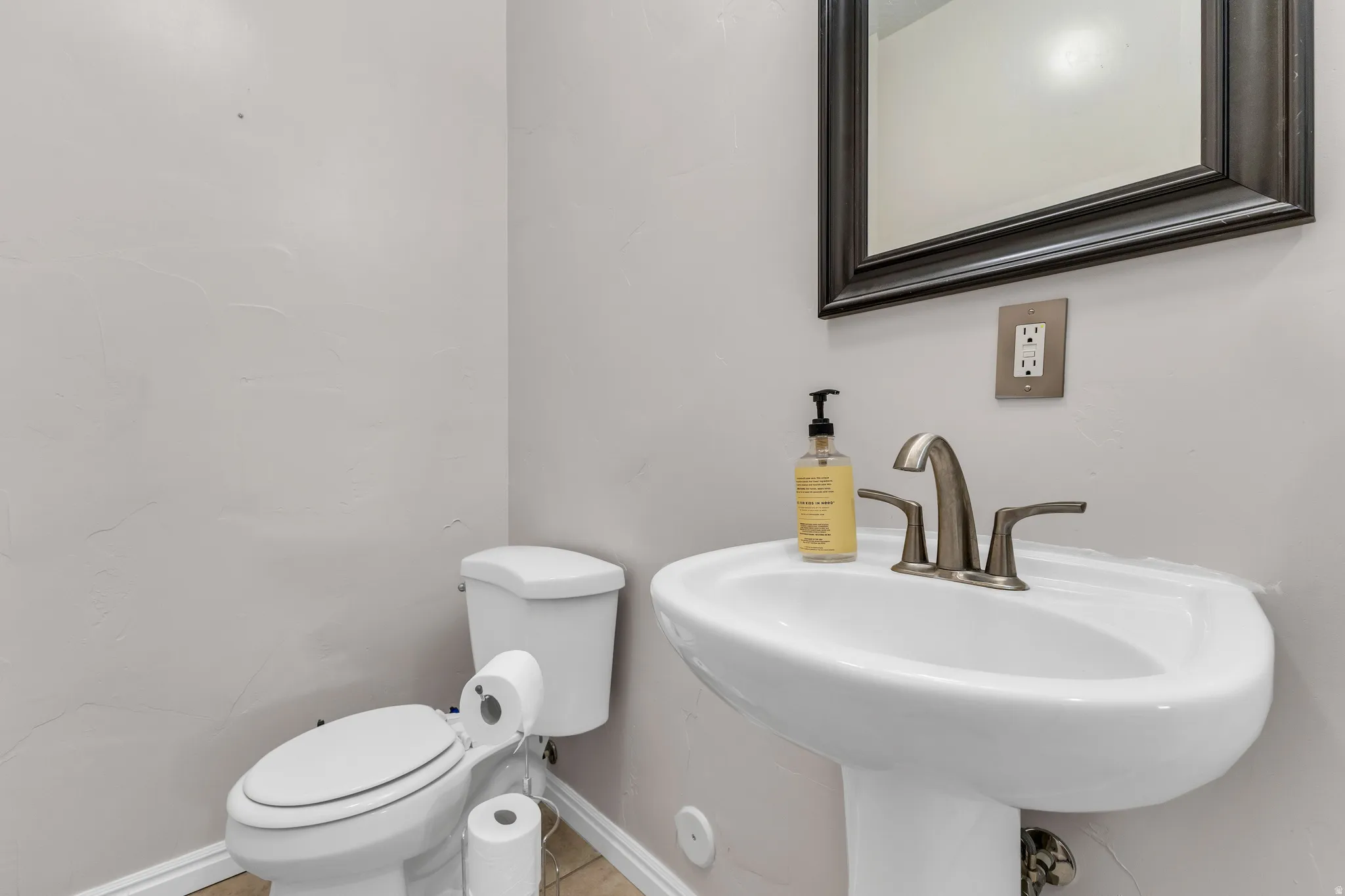 Pedestal sink with a brushed nickel faucet, framed mirror, and a white toilet
