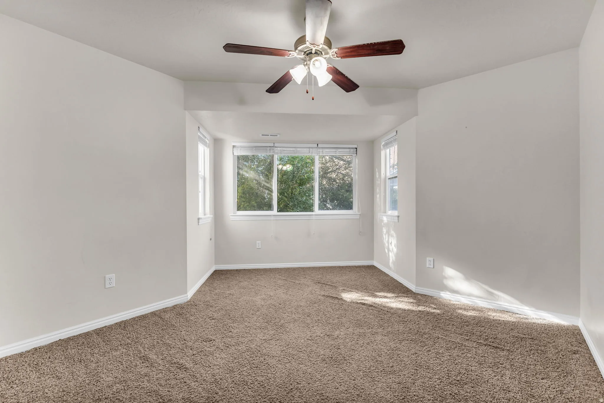 Recessed window alcove with multiple windows, ceiling fan with light fixture, and neutral carpeting