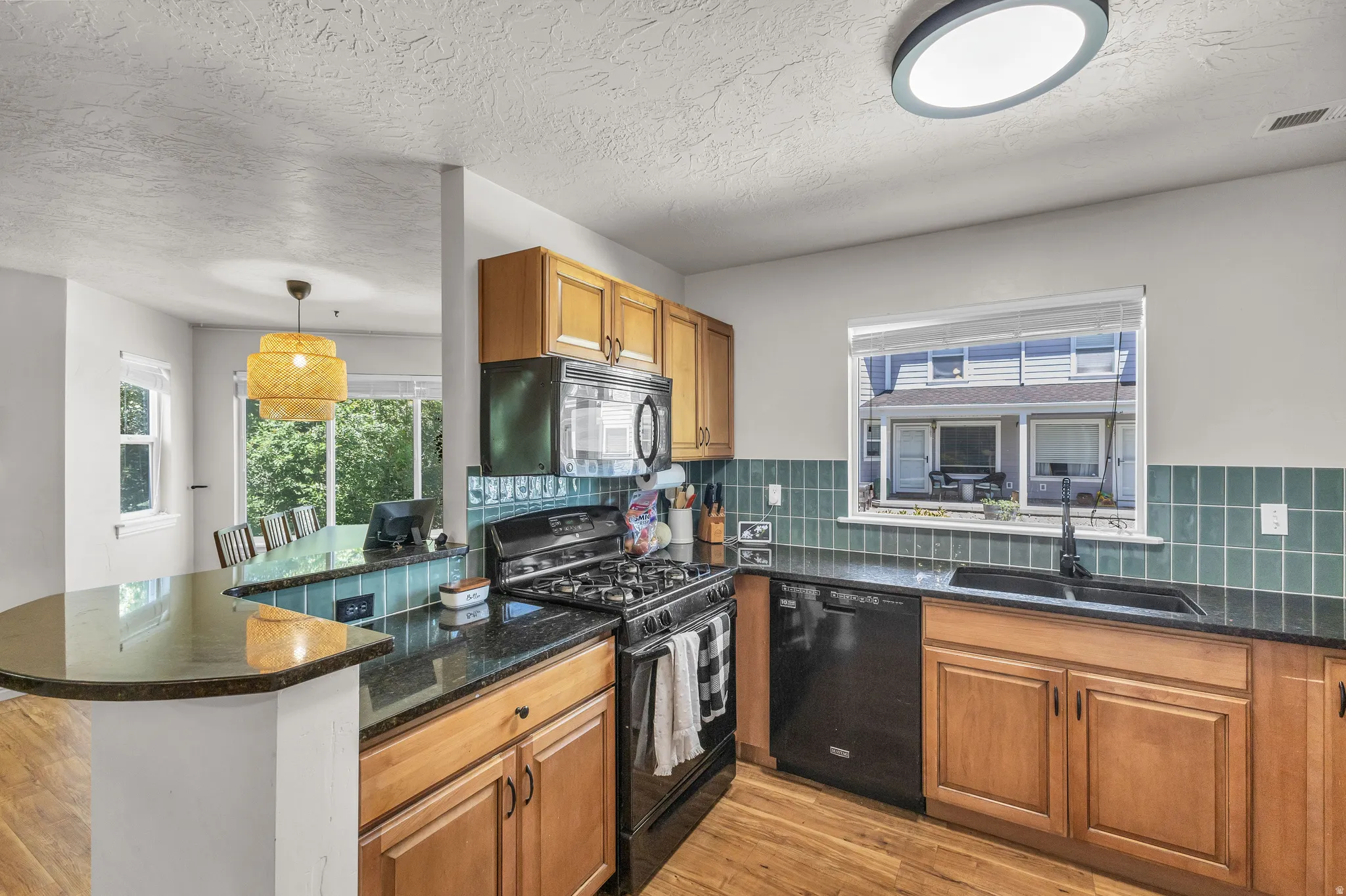 Kitchen featuring wood-finish cabinetry, black appliances, dark countertops, and a tiled backsplash