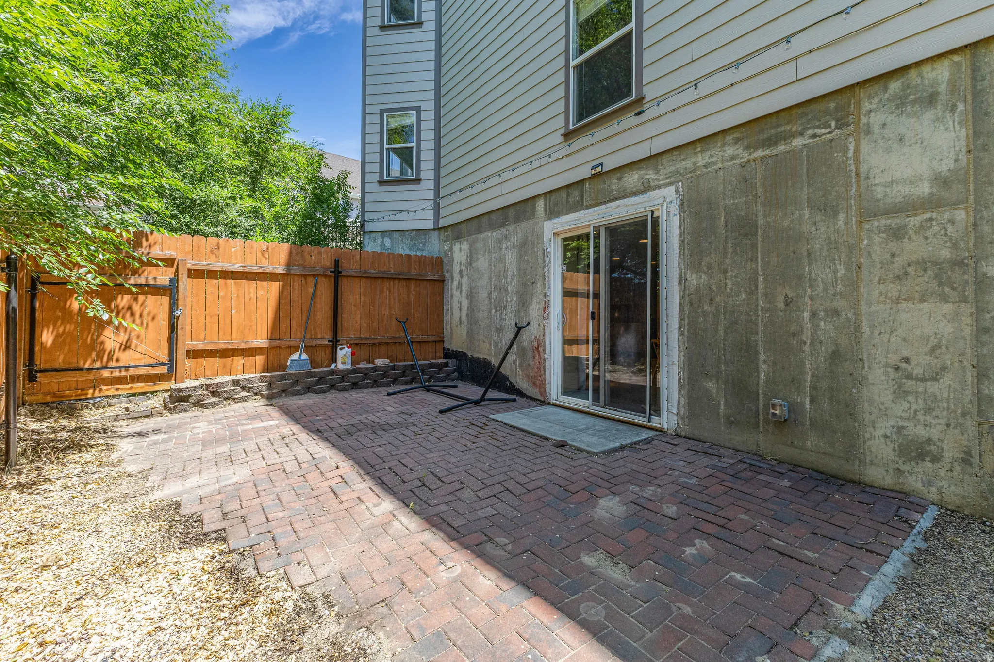Paved patio area featuring brick pavers, surrounded by gravel and a wood privacy fence with a gate