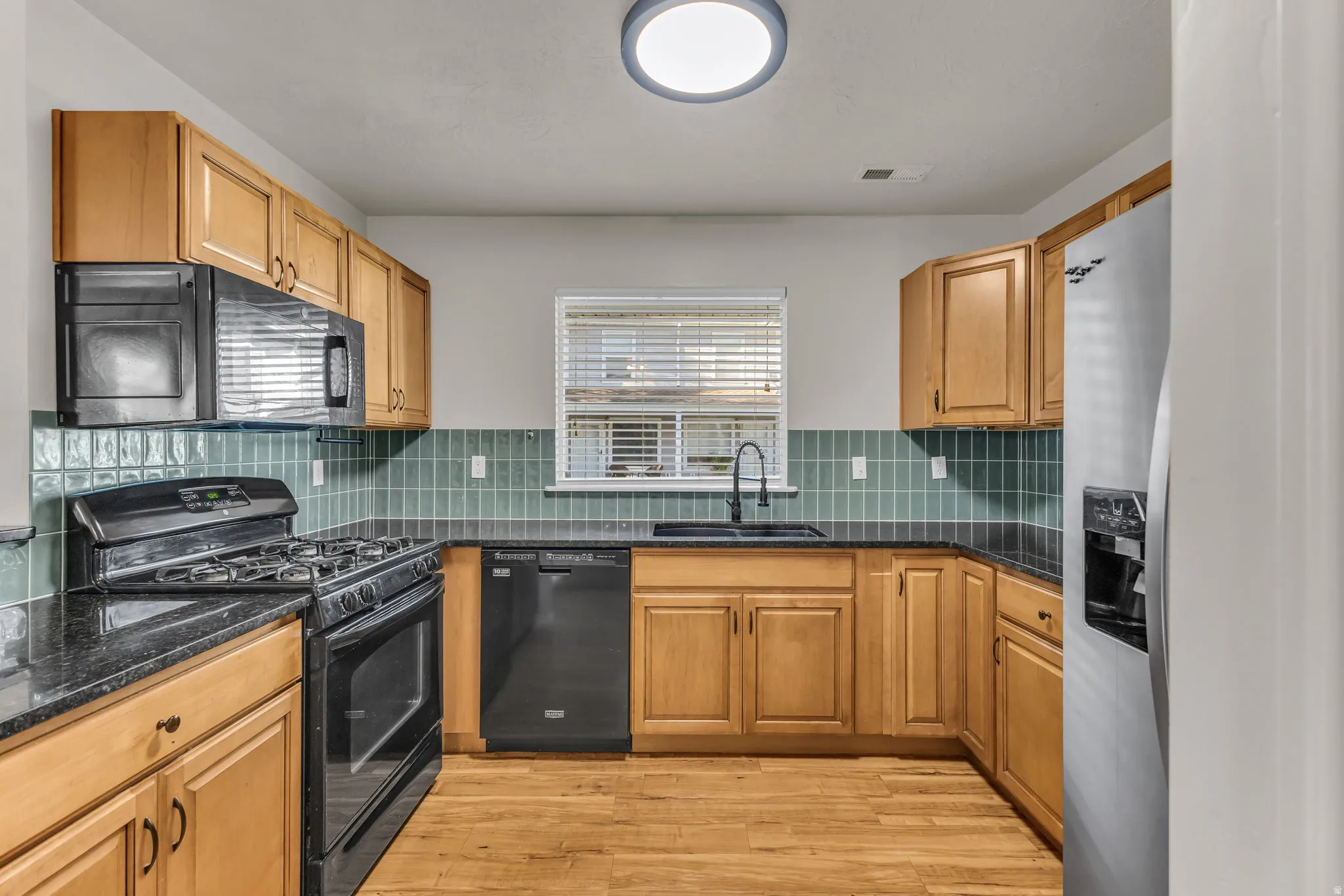 Kitchen featuring wood-finish cabinetry, black stone countertops, and a full suite of appliances