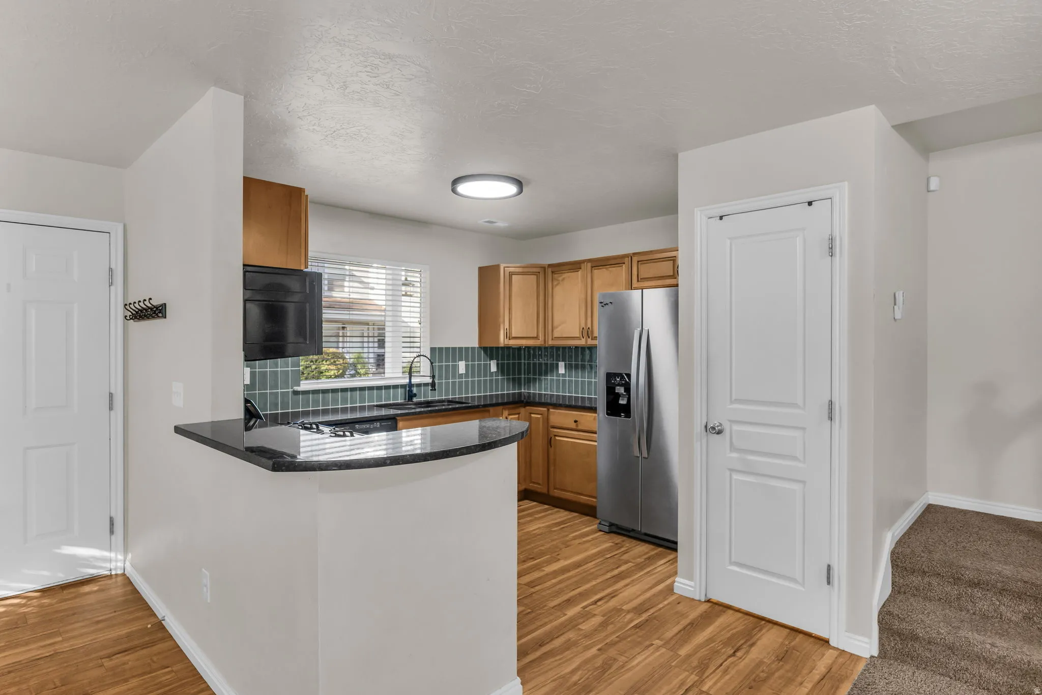Kitchen featuring wood-finish flooring, natural wood cabinetry, and a dark tile backsplash