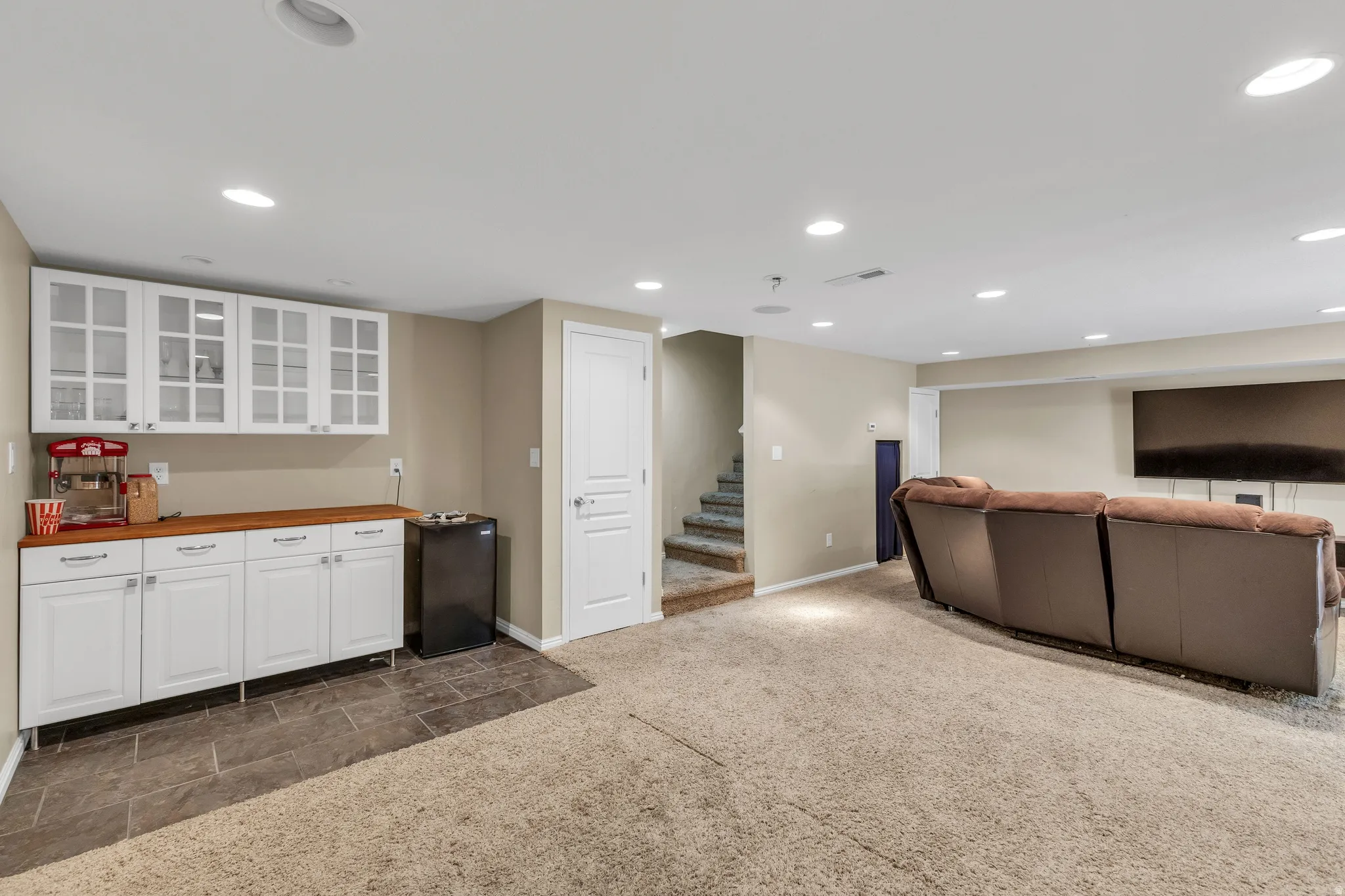 Recessed lighting, built-in cabinetry with glass-front uppers, wood-finish countertop, and durable tiled flooring