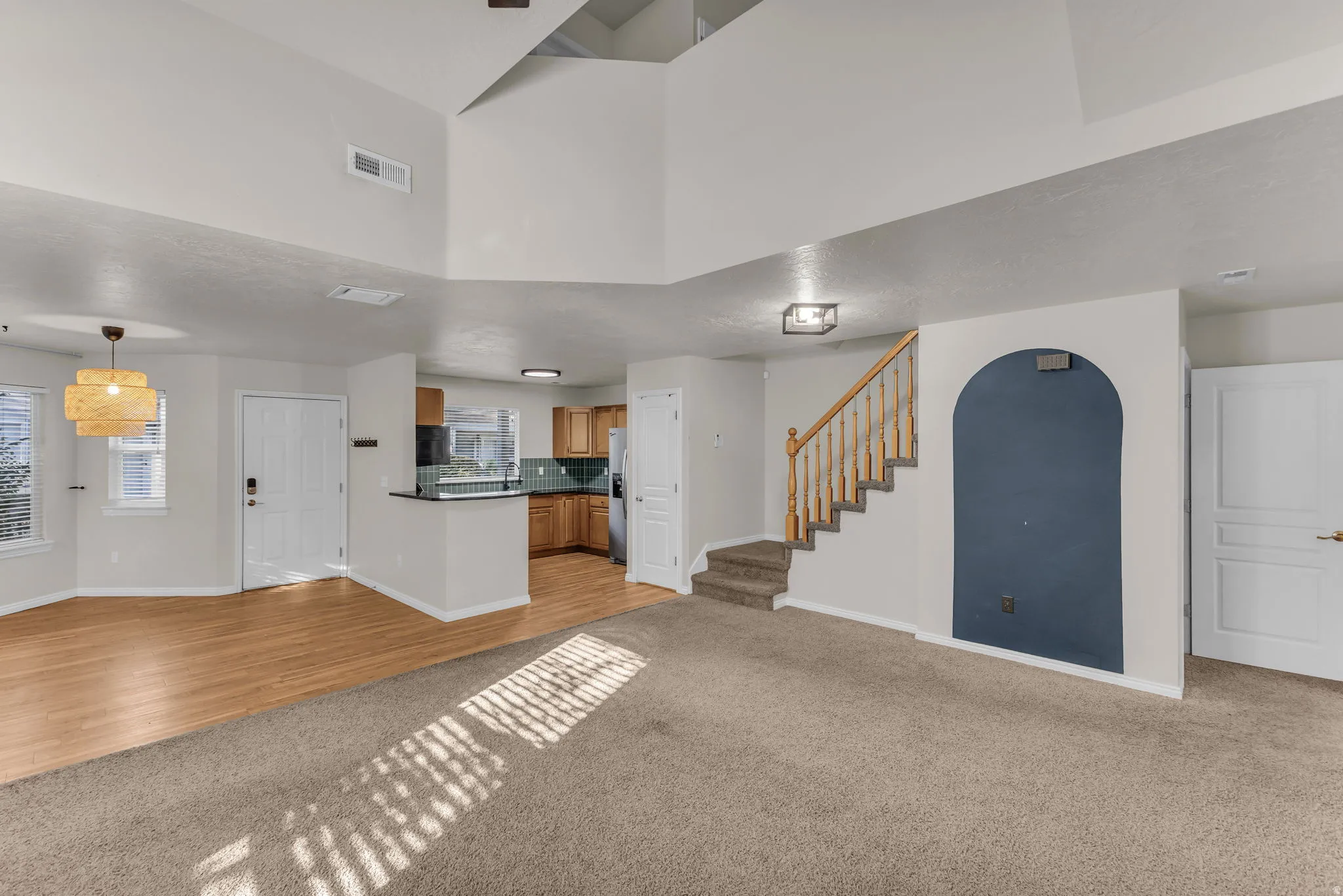 Vaulted ceilings, wood-finish flooring, staircase with natural wood banister, kitchen with wood cabinetry, and recessed lighting