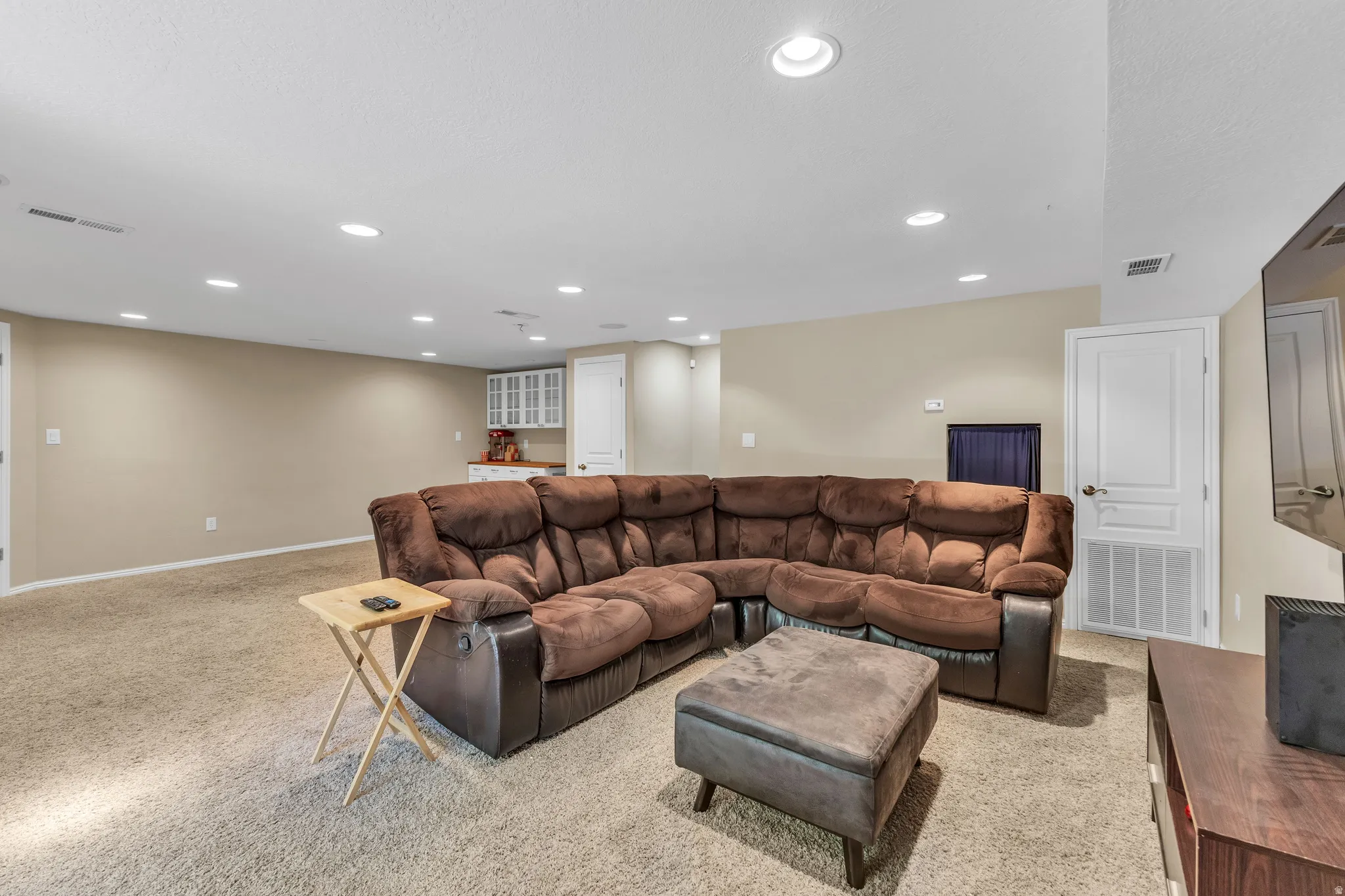 Recessed lighting illuminates the expansive carpeted living area with neutral wall tones