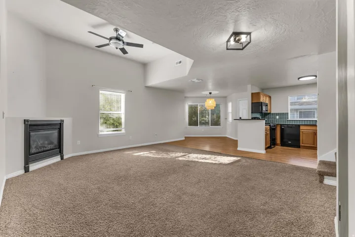 Vaulted ceiling with ceiling fan, built-in fireplace, wood-finish flooring, and kitchen with wood cabinetry and black appliances