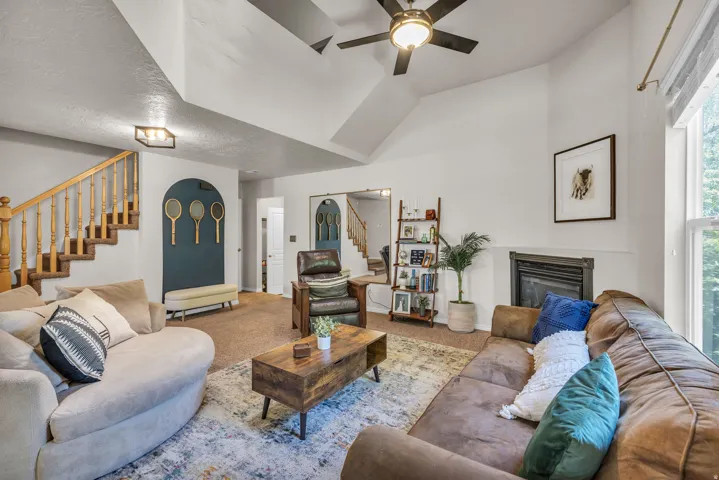 Vaulted ceilings with ceiling fan, built-in fireplace, wood staircase with balusters, large window, and wall-mounted light fixtures