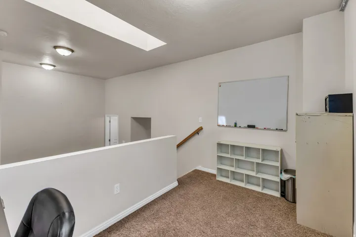 Skylight, two flush-mount ceiling lights, light brown carpet, and a white wall with wood handrail