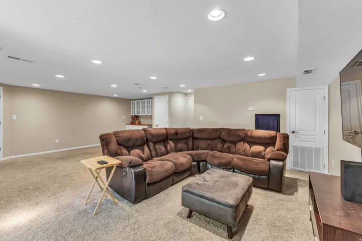 Recessed lighting illuminates the expansive carpeted living area with neutral wall tones