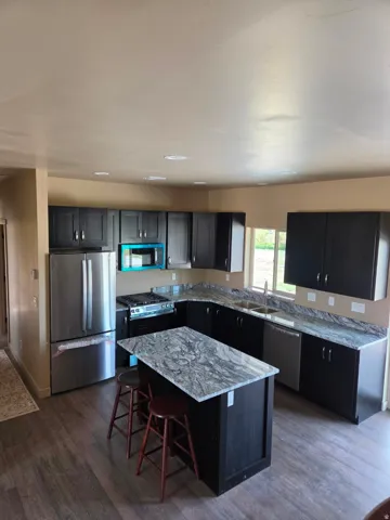Kitchen featuring dark cabinetry, stainless steel appliances, a center island with a stone countertop, coordinating perimeter stone countertops, and wood-finish flooring