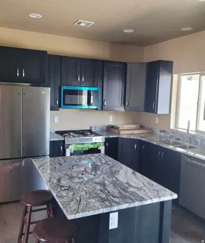 Kitchen featuring dark cabinetry, stainless steel appliances, granite countertops, and an island with seating