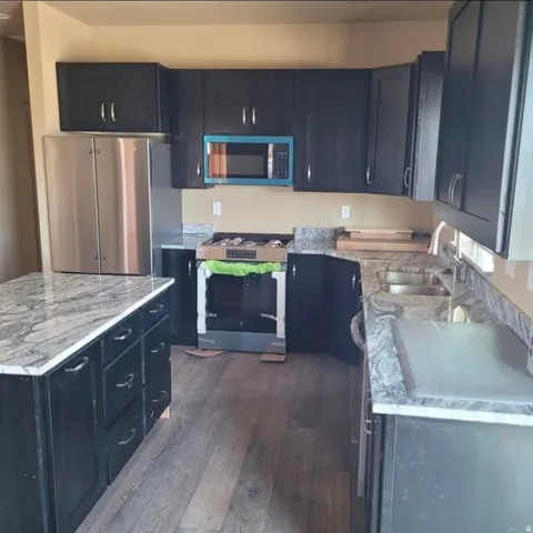 Wood-finish flooring with dark cabinetry, stainless steel appliances, and light-toned countertops