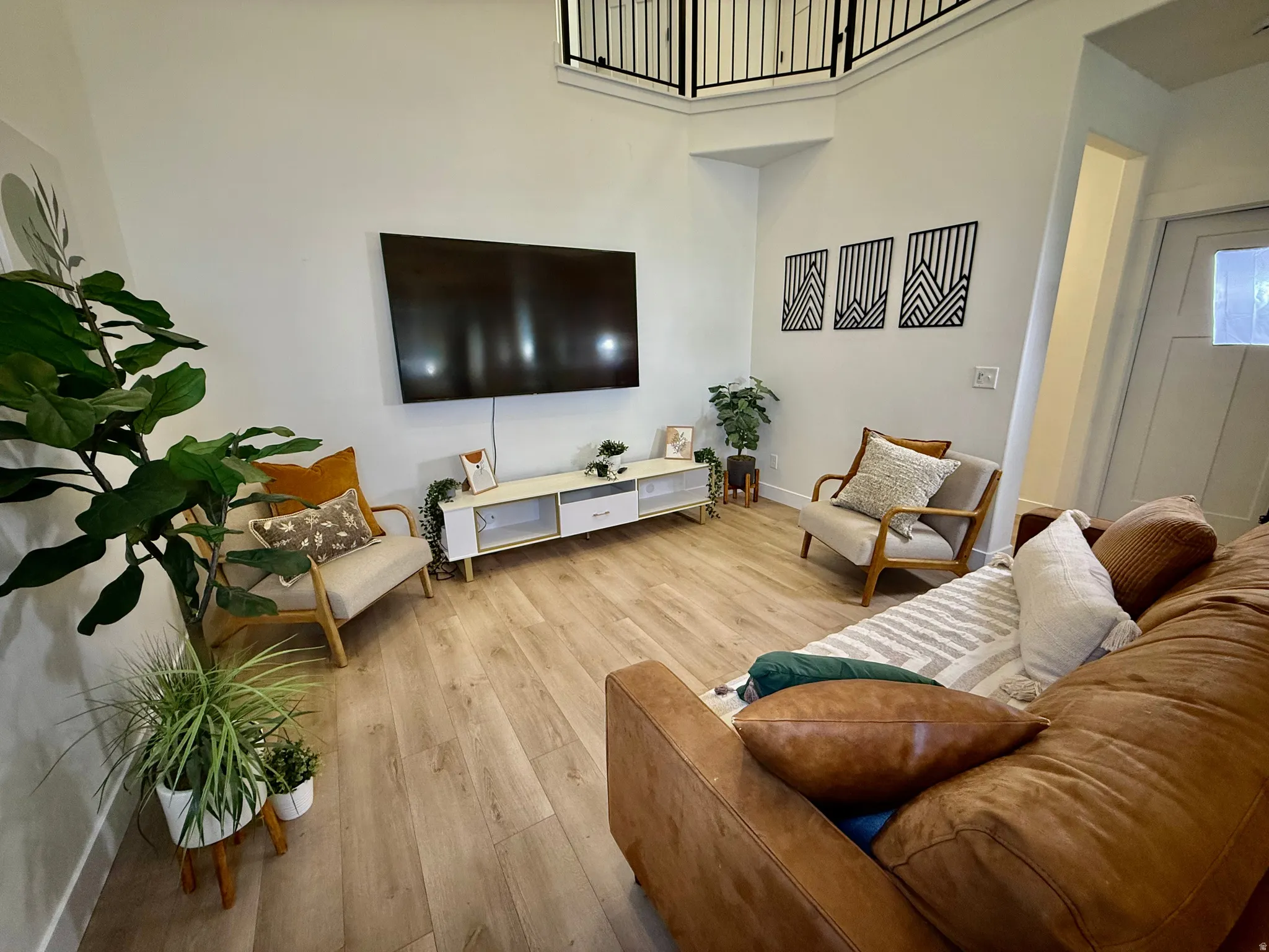 Vaulted ceiling, wood-finish flooring, white walls, black iron railing, and white media console