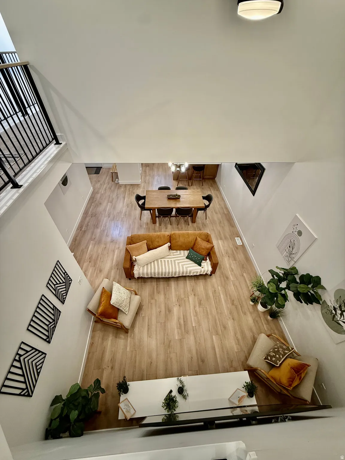 Spacious open-concept living area featuring wood-finish flooring, a two-story ceiling, and a modern black metal staircase railing