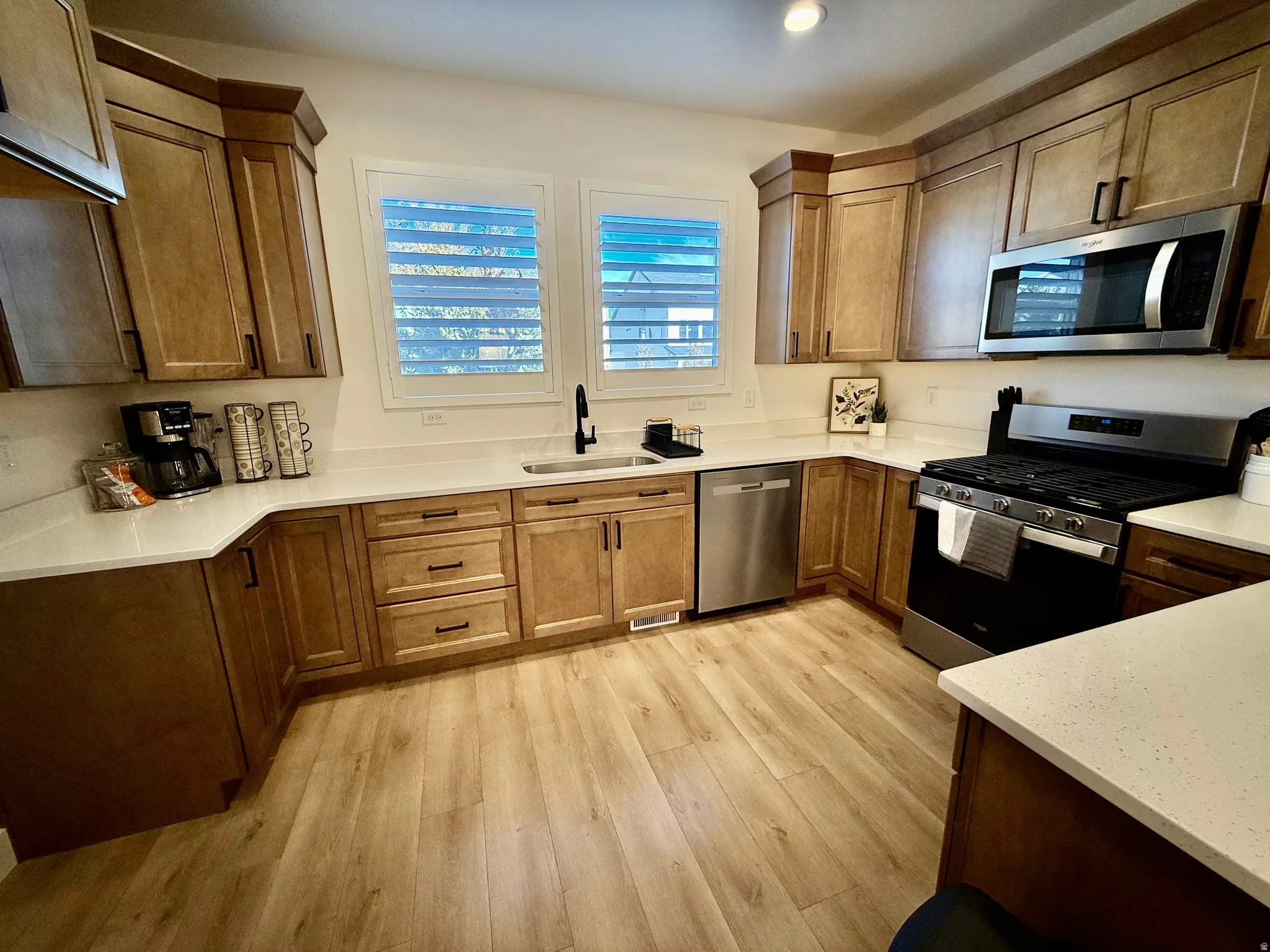 U-shaped kitchen featuring wood-finish cabinetry, stainless steel appliances, solid surface countertops, and wood-finish flooring