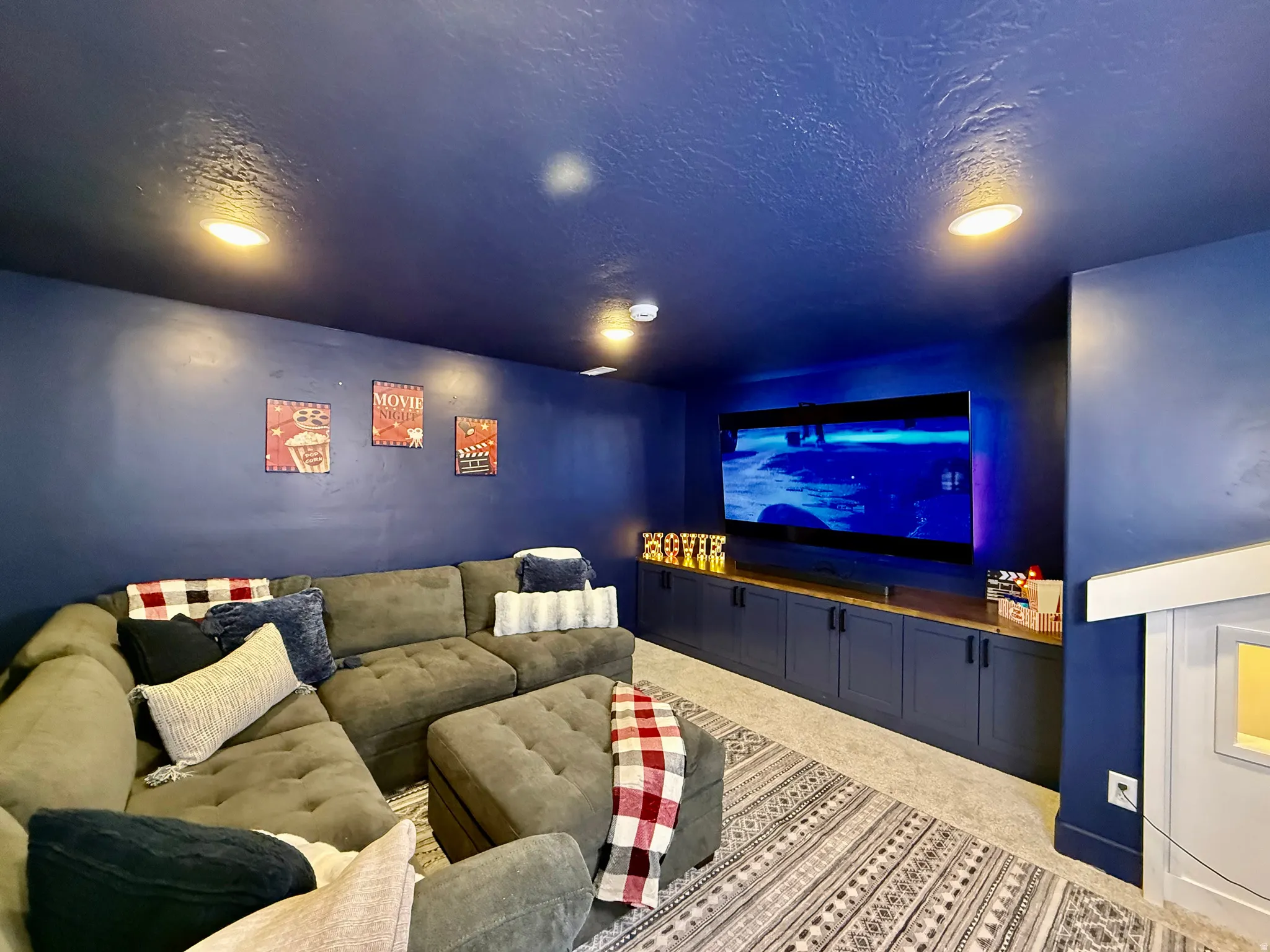 Recessed lighting illuminates a carpeted floor, built-in lower cabinetry with a wood-finish countertop, and a wall-mounted display