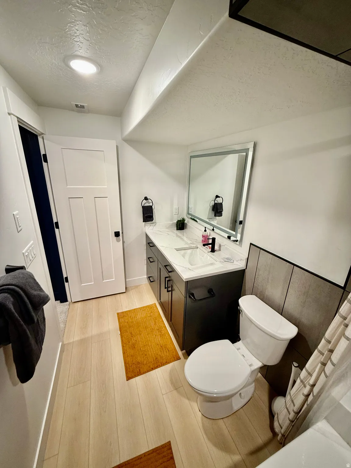 Wood-finish flooring, dual-sink vanity with white countertop, chrome-framed mirror, and recessed ceiling lighting