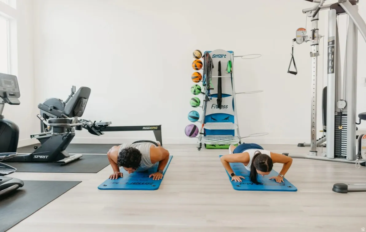 Fitness room with light wood-finish flooring, white walls, and various exercise equipment